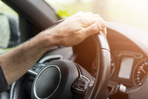 Male hands holding and turning a car steering wheel.