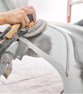 Technician sanding car bumper as part of collision repair process at auto body shop