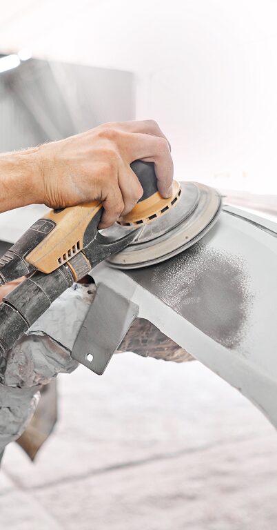 Technician sanding car bumper as part of collision repair process at auto body shop